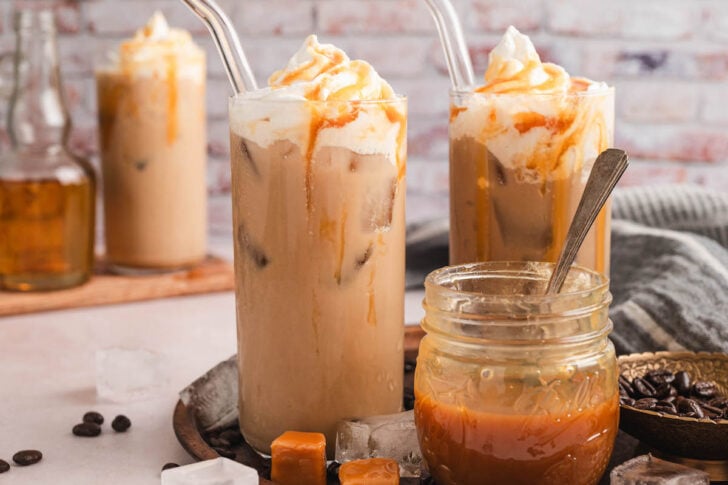 Two glasses of iced caramel coffee on a tray with a jar of caramel sauce.