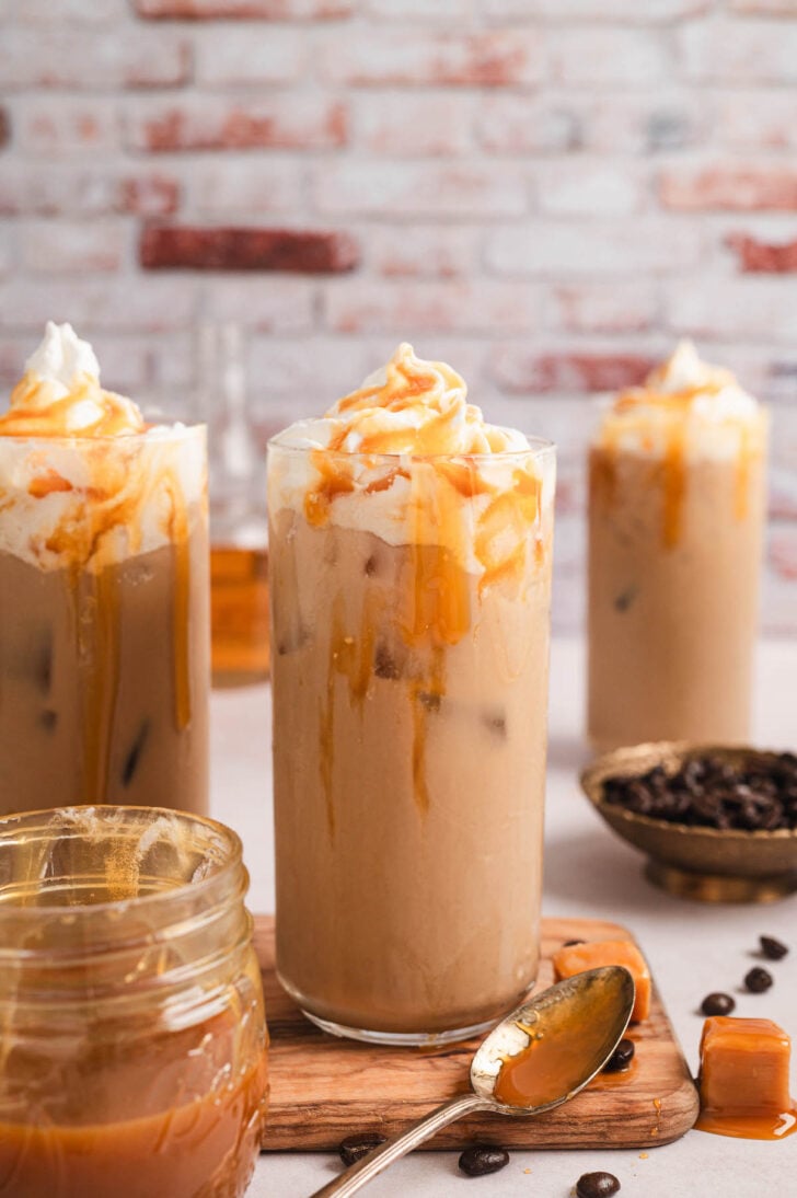 A tall glass of caramel iced coffee in front of a textured brick wall.