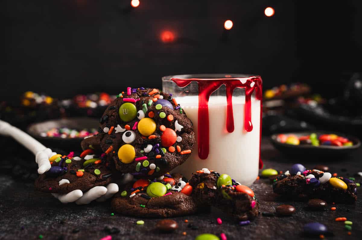 A Halloween cookie resting against a glass of milk decorated with fake blood.