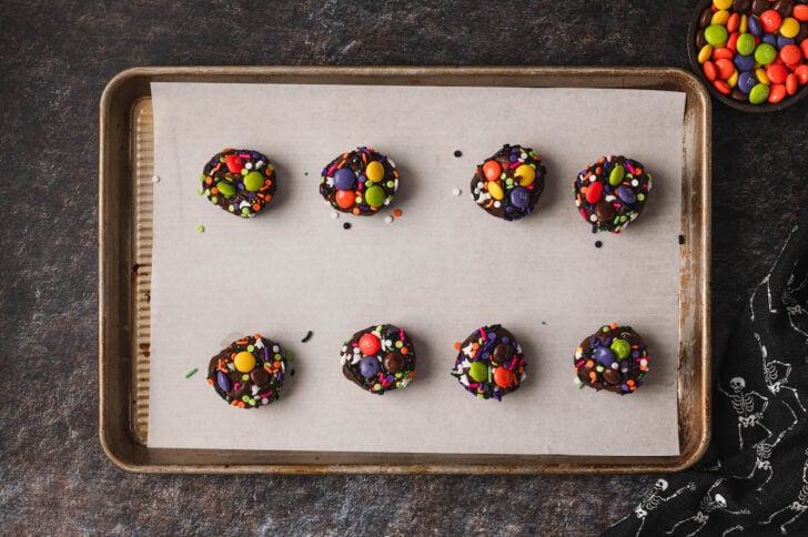 Chocolate cookie dough balls rolled in sprinkles and colored candies on a rimmed baking pan.