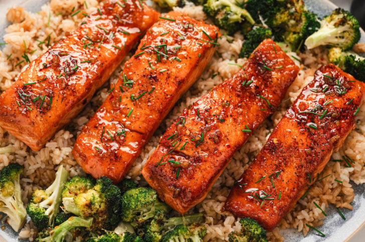 Four pieces of a honey salmon recipe on a platter, served over rice and broccoli.