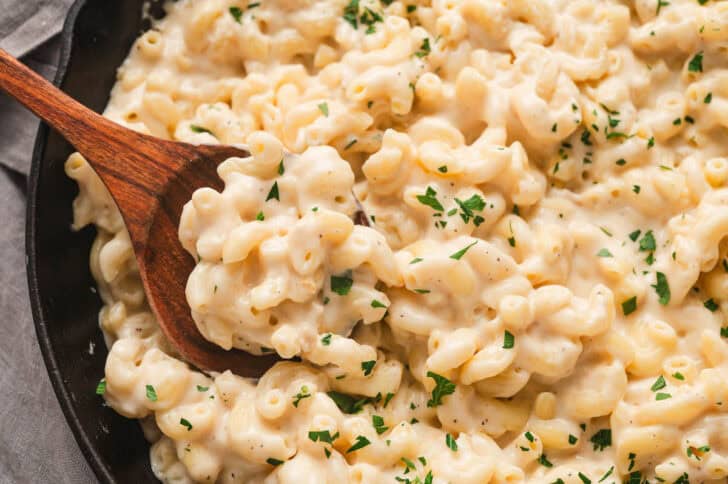 A wooden spoon stirring homemade stovetop mac and cheese.