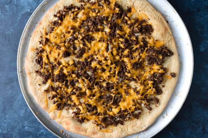 A burger pizza topped with cheese on a round pan.