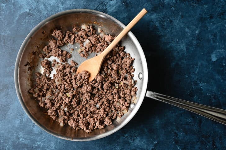 Ground beef being cooked in a stainless steel skillet.