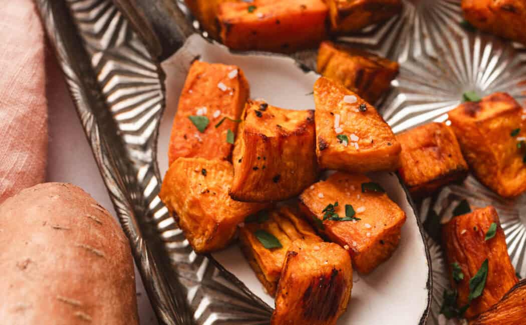 Oven roasted sweet potatoes on a serving spoon on a textured baking pan.