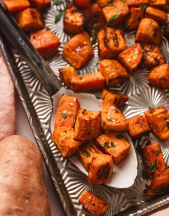 Oven roasted sweet potatoes on a serving spoon on a textured baking pan.