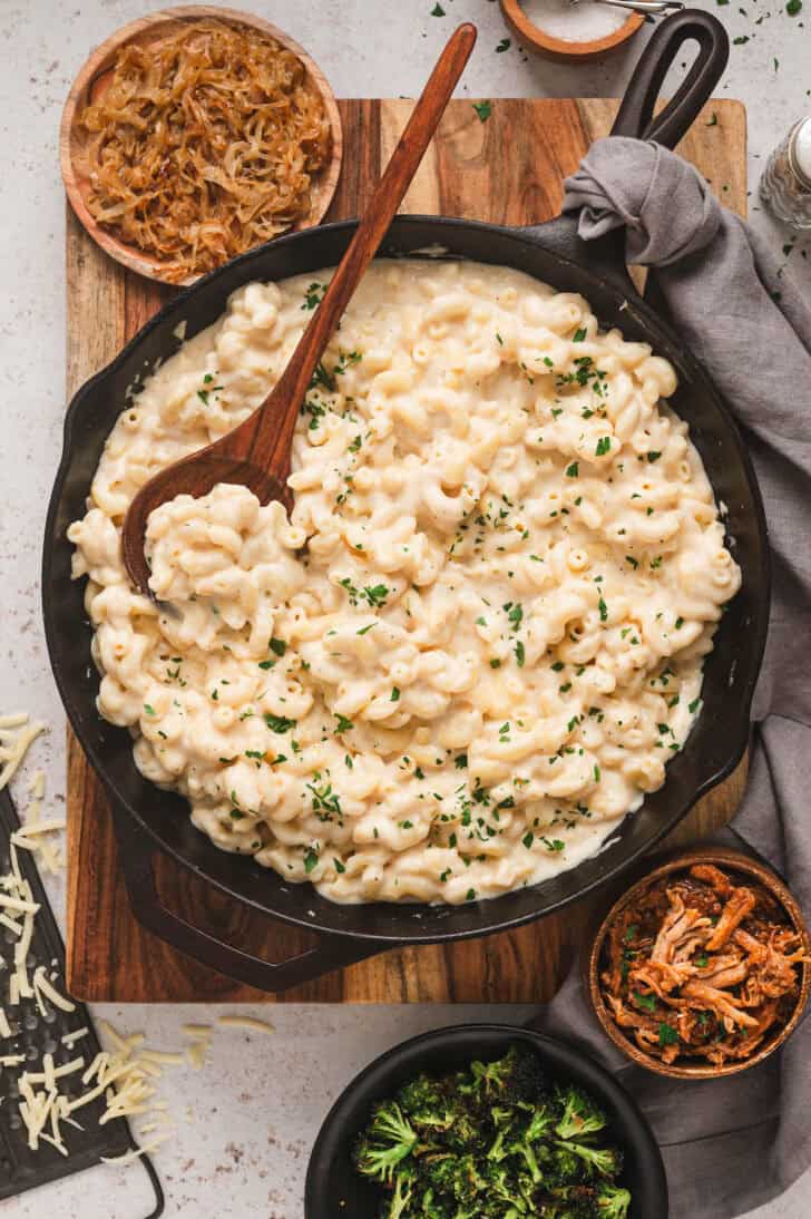 Stovetop mac and cheeses in a cast iron skillet, surrounded by various mix-in ingredients.