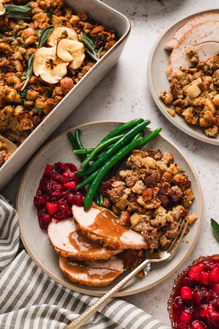 A holiday dinner plate filled with sausage and apple stuffing, turkey and gravy, cranberry sauce and green beans.