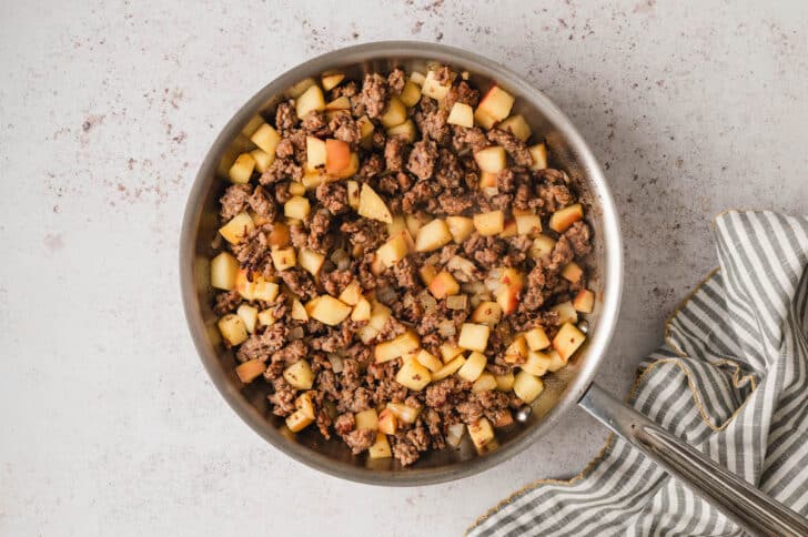 A mixture of ground sausage and apples in a skillet.