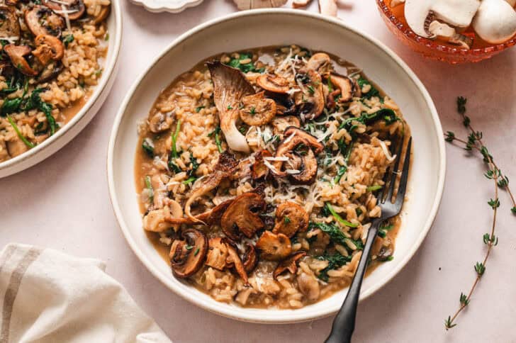 A bowl of creamy mushroom risotto with a black fork in it.