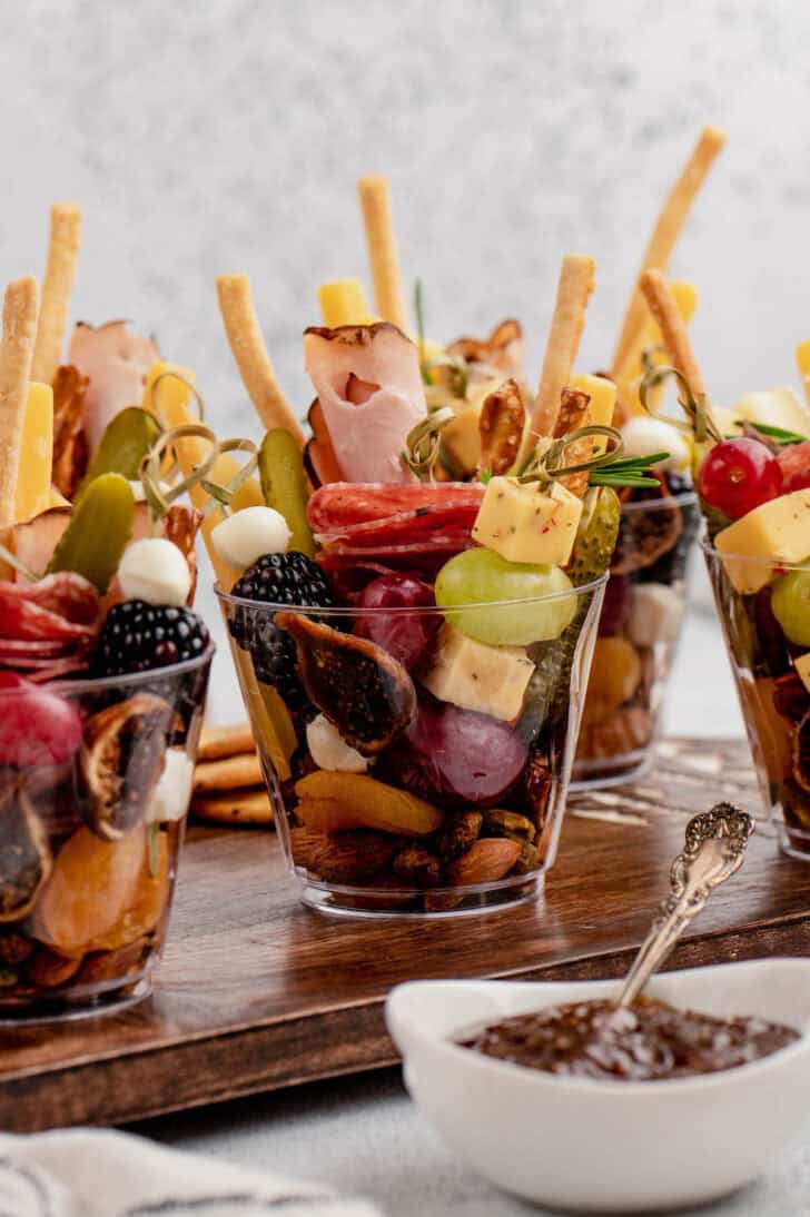 Small glasses filled with various snacks on a wooden serving board.