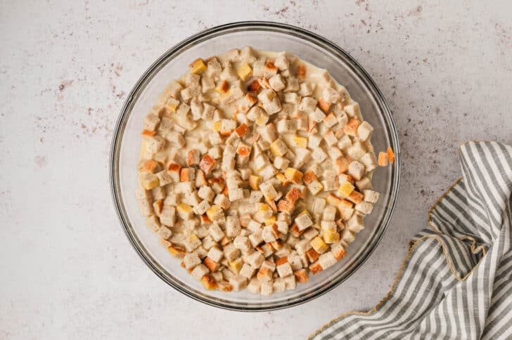 Dried bread cubes soaking in liquid in a glass bowl.