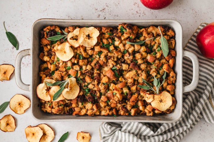 Sausage apple stuffing garnished with dried apples and fresh age in a rectangle baking dish.