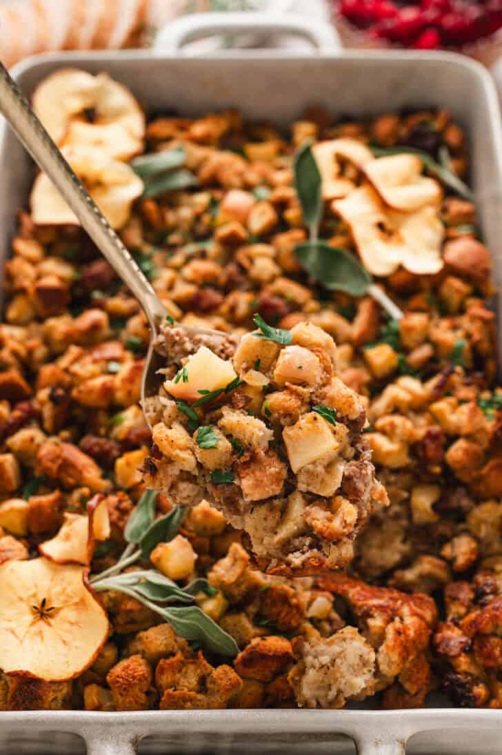 A spoon lifting a serving of an apple stuffing recipe from a baking dish.