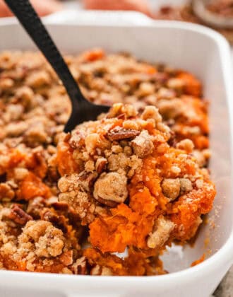 A black spoon lifting a scoop of easy sweet potato casserole out of a white baking dish.