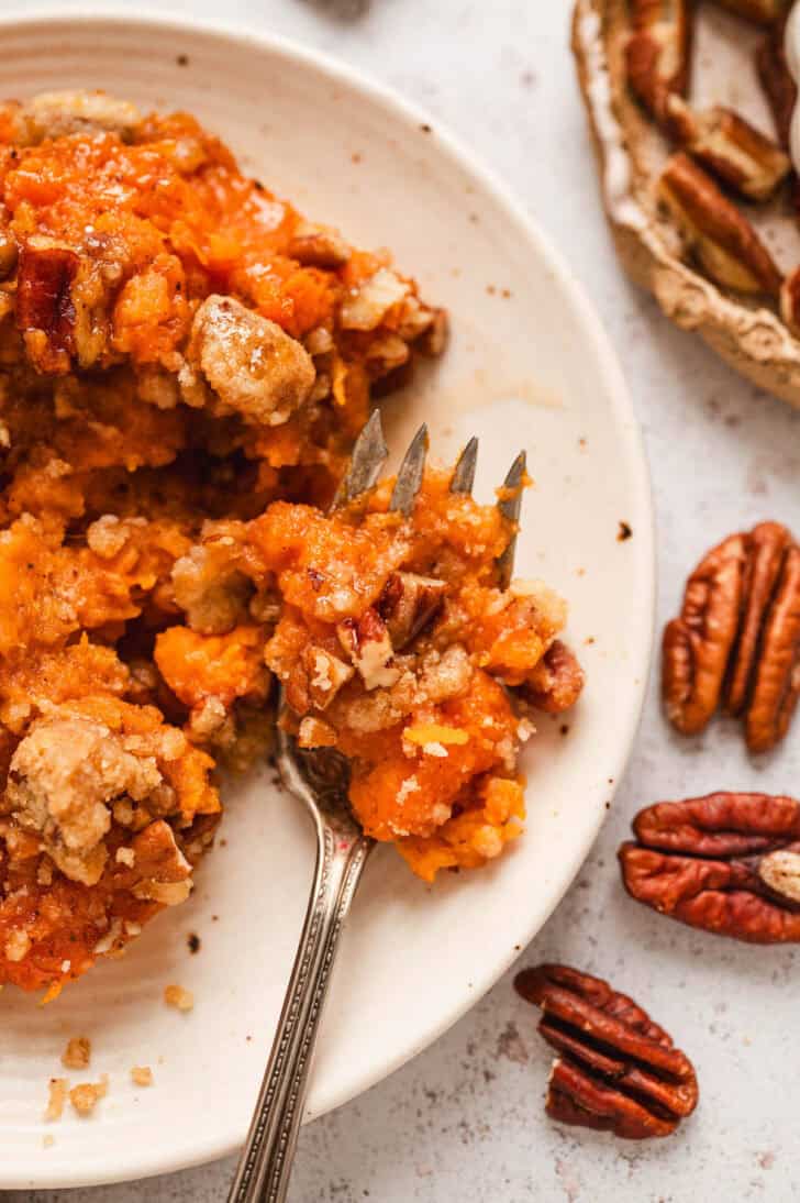 A fork showing some of the recipe for sweet potato casserole on a white plate.