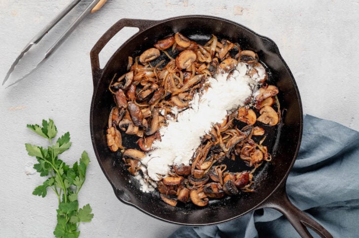 Flour sprinkled over browned mushrooms and onions in a skillet.