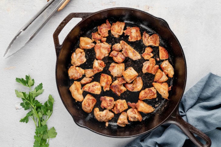 Poultry cubes being browned in a cast iron skillet.