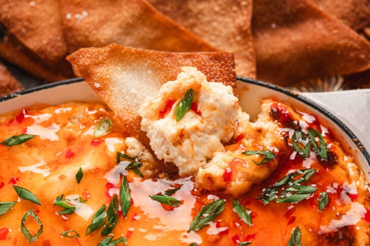 A wonton chip dipping into an easy crab rangoon dip recipe.