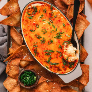 A dish of crab rangoon dip on a tray with wonton chips.