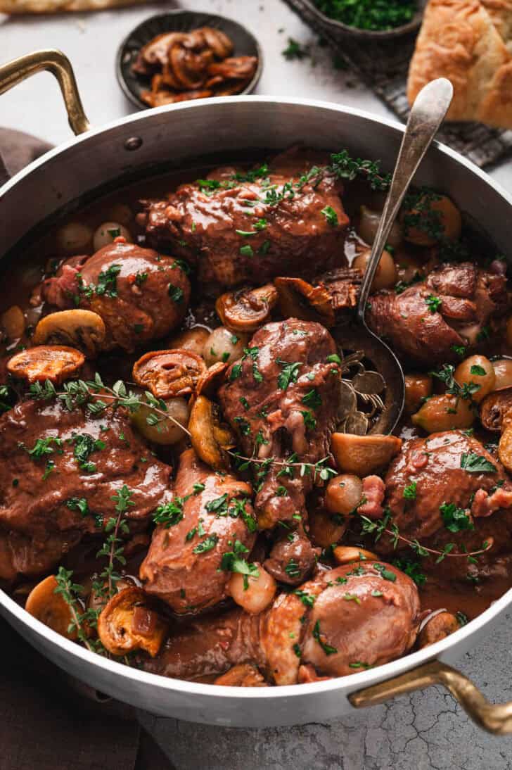 A coq au vin recipe in a stainless steel pot.