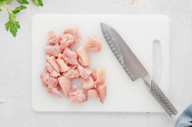 Raw poultry cubes on a white cutting board.