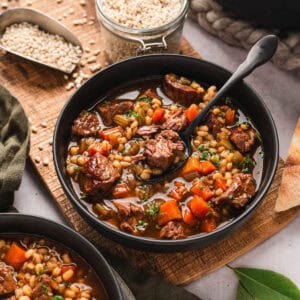 A bowl of a beef barley soup recipe with a spoon in it.