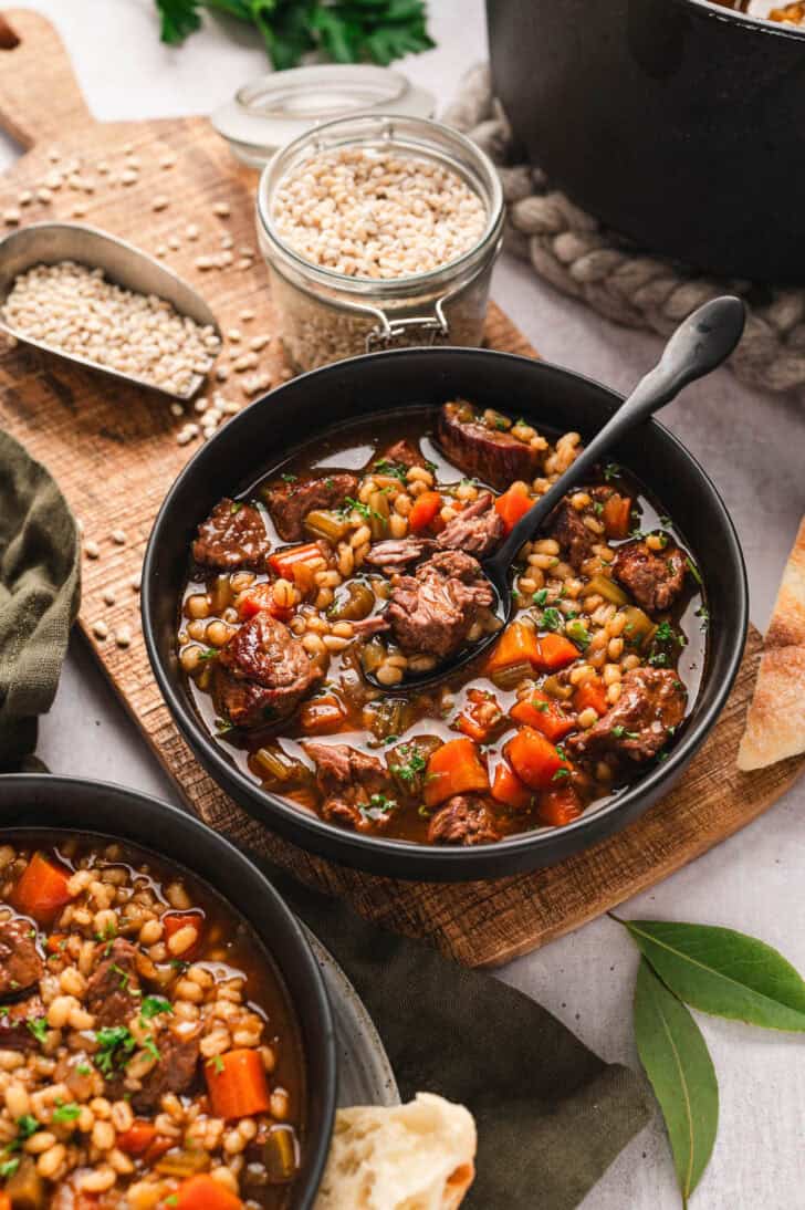 A bowl of a beef barley soup recipe with a spoon in it.