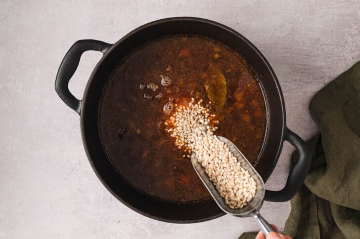 Grains being added to a soup mixture in a Dutch oven.