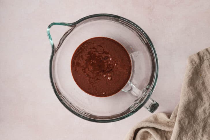 A glass stand mixer bowl filled with a brown mixture.