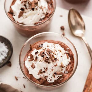 Two small glass dishes filled with easy chocolate mousse, topped with whipped cream and chocolate shavings.