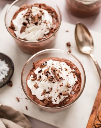 Two small glass dishes filled with easy chocolate mousse, topped with whipped cream and chocolate shavings.