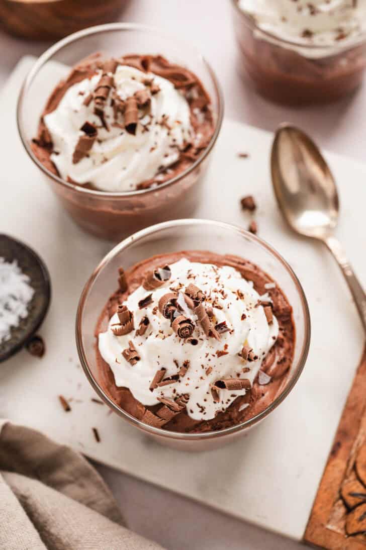 Two small glass dishes filled with easy chocolate mousse, topped with whipped cream and chocolate shavings.