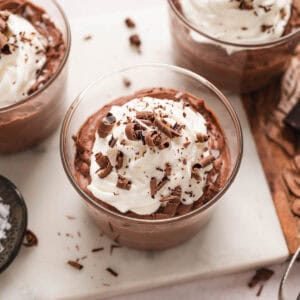 Two small glass dishes filled with easy chocolate mousse, topped with whipped cream and chocolate shavings.