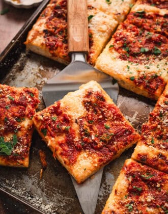 A slice of grandma pizza being lifted from a pan.