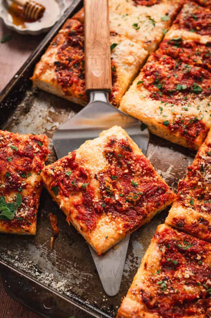 A slice of grandma pizza being lifted from a pan.