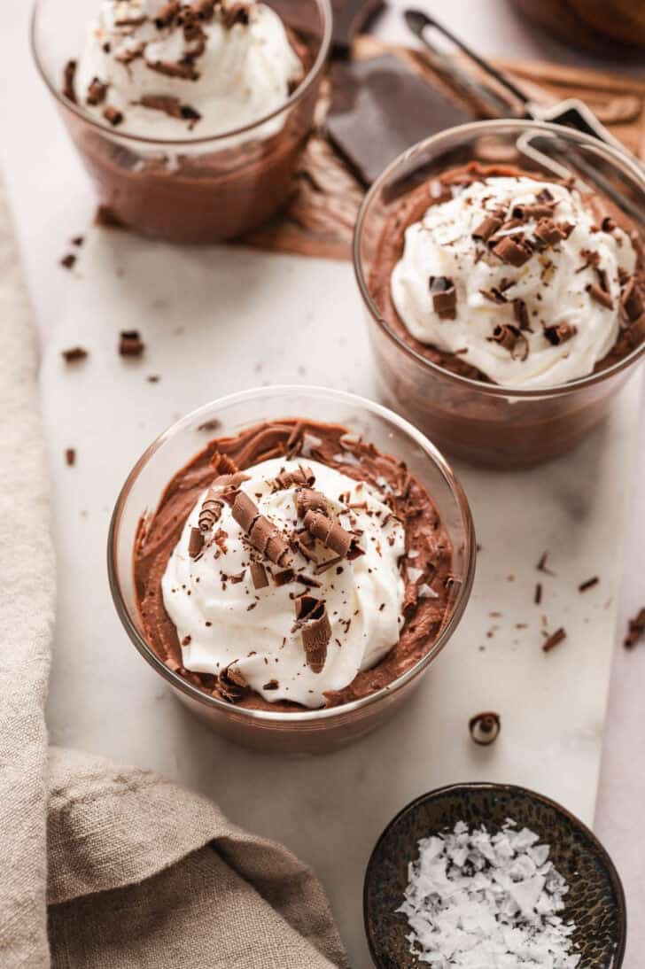 Three small glass dishes filled with the best chocolate mousse recipe, topped with whipped cream and chocolate shavings.