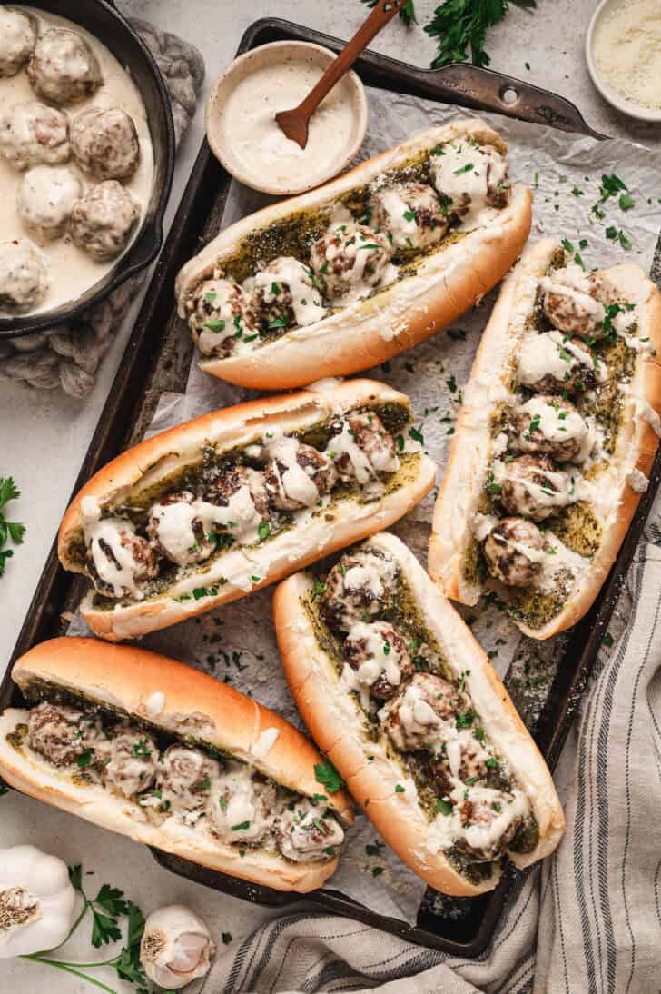 Five meatball sandwiches on a rimmed baking pan.