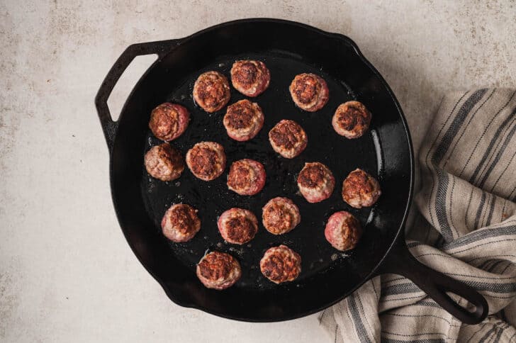 The meatballs for a meatball subs recipe being browned in a cast iron skillet.