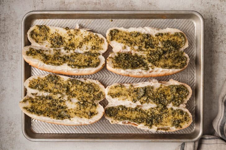 Sub rolls spread with pesto on a rimmed baking pan.