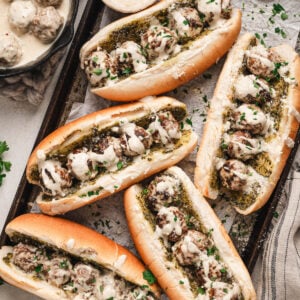 Five meatball sandwiches on a rimmed baking pan.