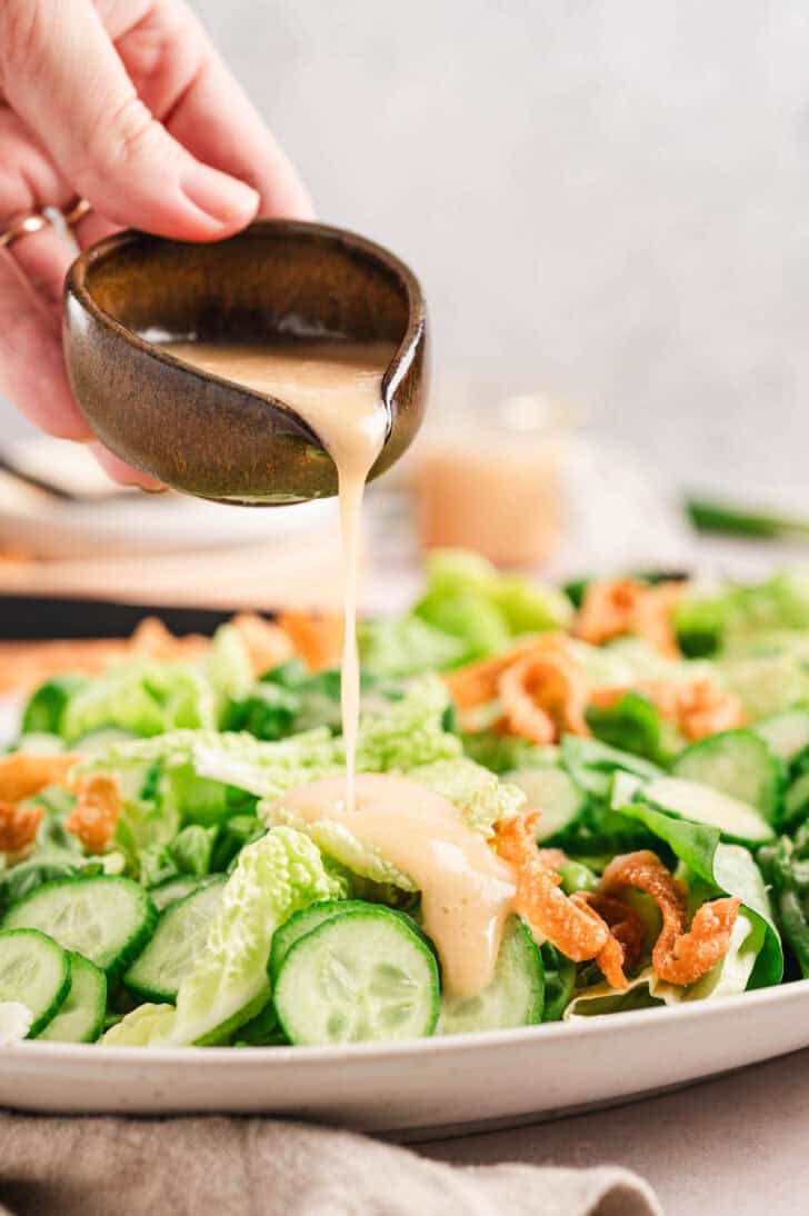 A hand pouring a vinaigrette over a green salad.