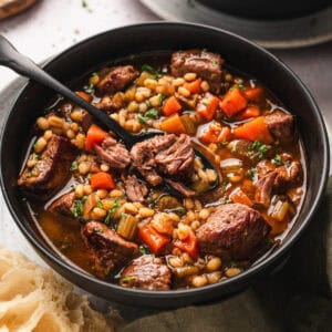 A bowl of a beef barley soup recipe with a spoon in it.