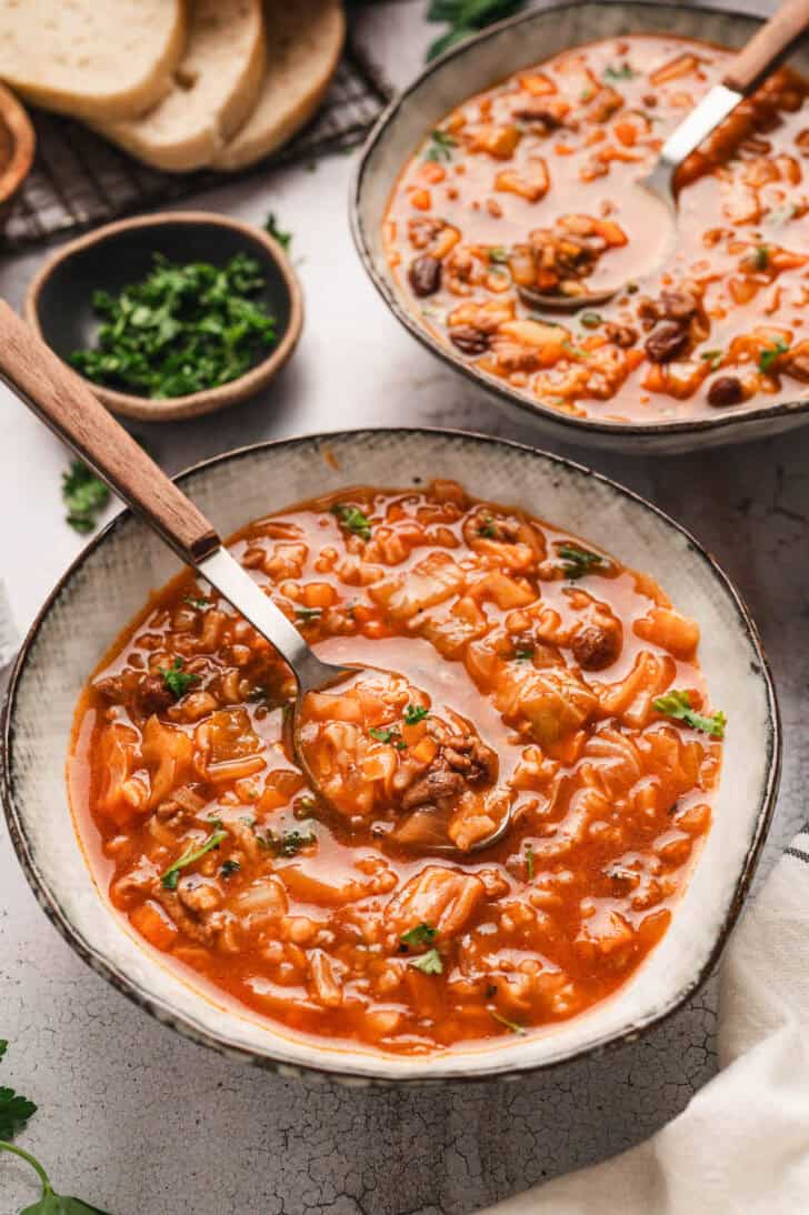 Two bowls of a cabbage roll soup recipe with spoons in them.