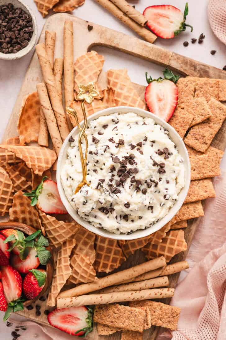 A bowl of cannoli dip on a platter with waffle pieces, graham crackers and strawberries.