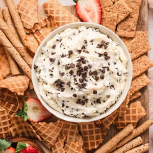 A bowl of cannoli dip on a platter with waffle pieces, graham crackers and strawberries.