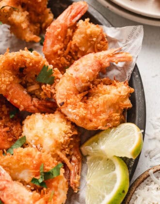 A finished coconut shrimp recipe being served with lime wedges.