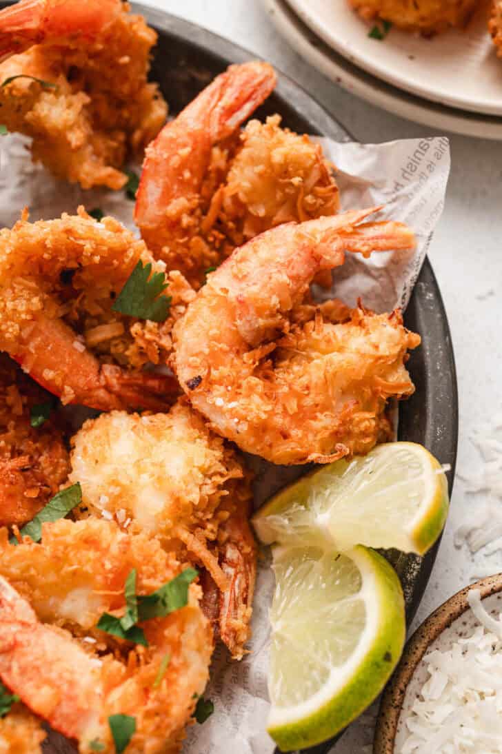 A finished coconut shrimp recipe being served with lime wedges.