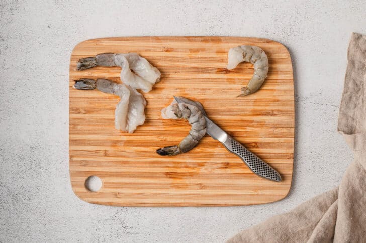 Prawns being butterflied on a wooden cutting board.