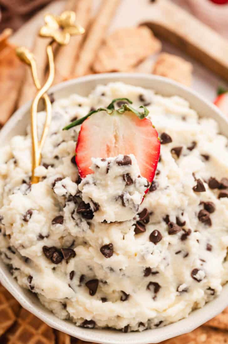 A bowl of easy cannoli dip with a strawberry dipping into it.